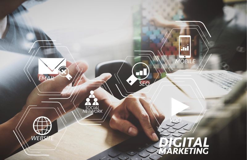 Persona usando laptop y smartphone con iconos de SEO, email y marketing digital sobre la pantalla.